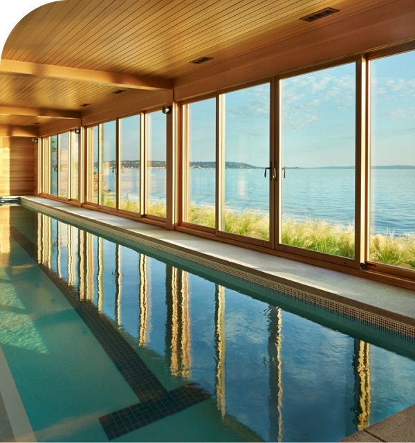 Indoor lap pool with wood-paneled walls and floor-to-ceiling windows from a premium window and door company overlooking the ocean.