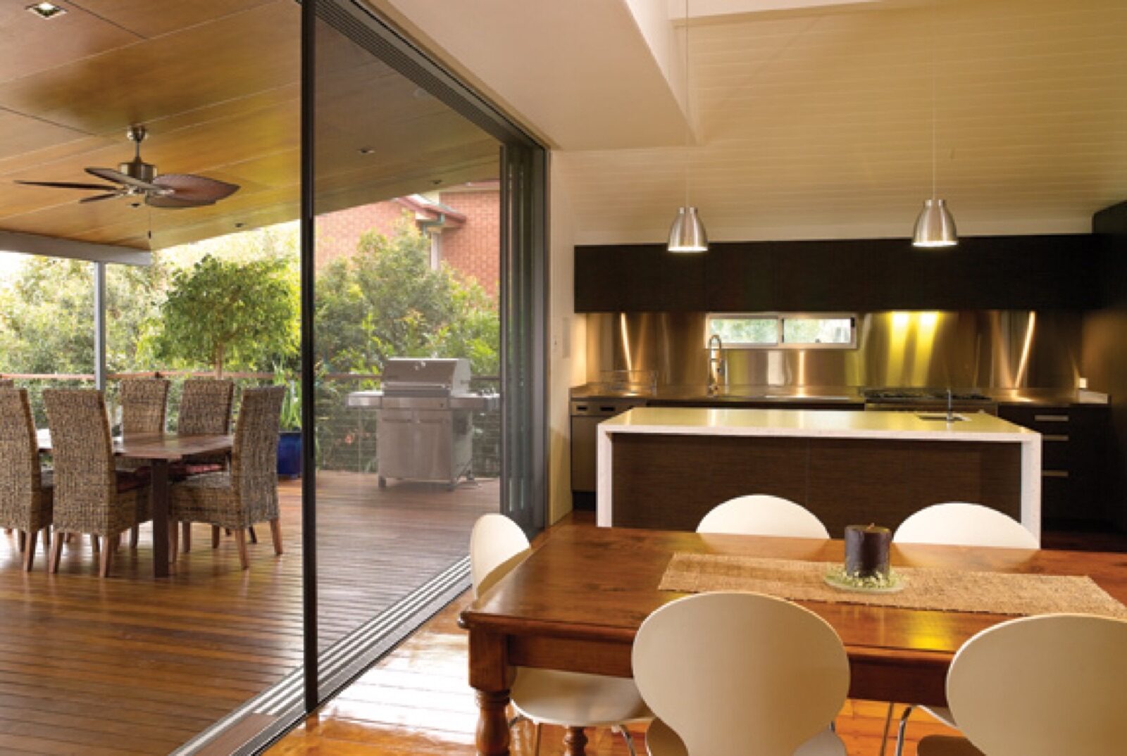 Modern kitchen and dining area with Centor doors opening onto a wooden deck with an outdoor dining table and grill.