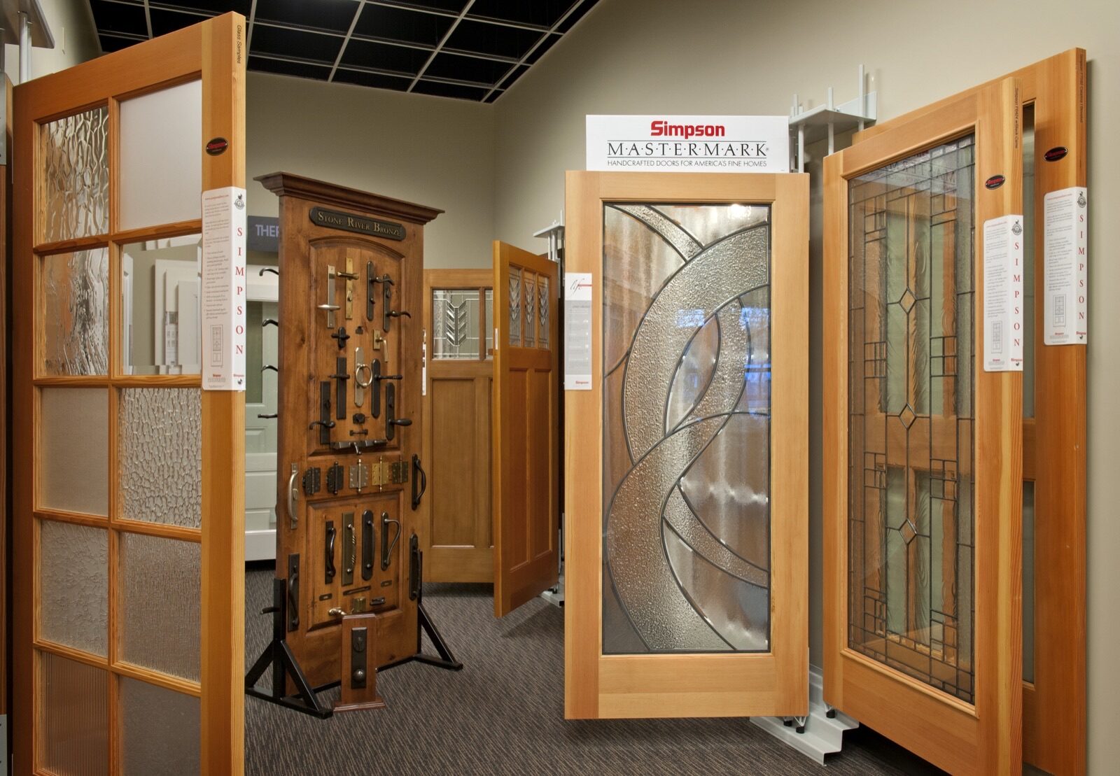 A display room showcasing various Simpson doors with decorative glass panels and a sample board of door hardware.