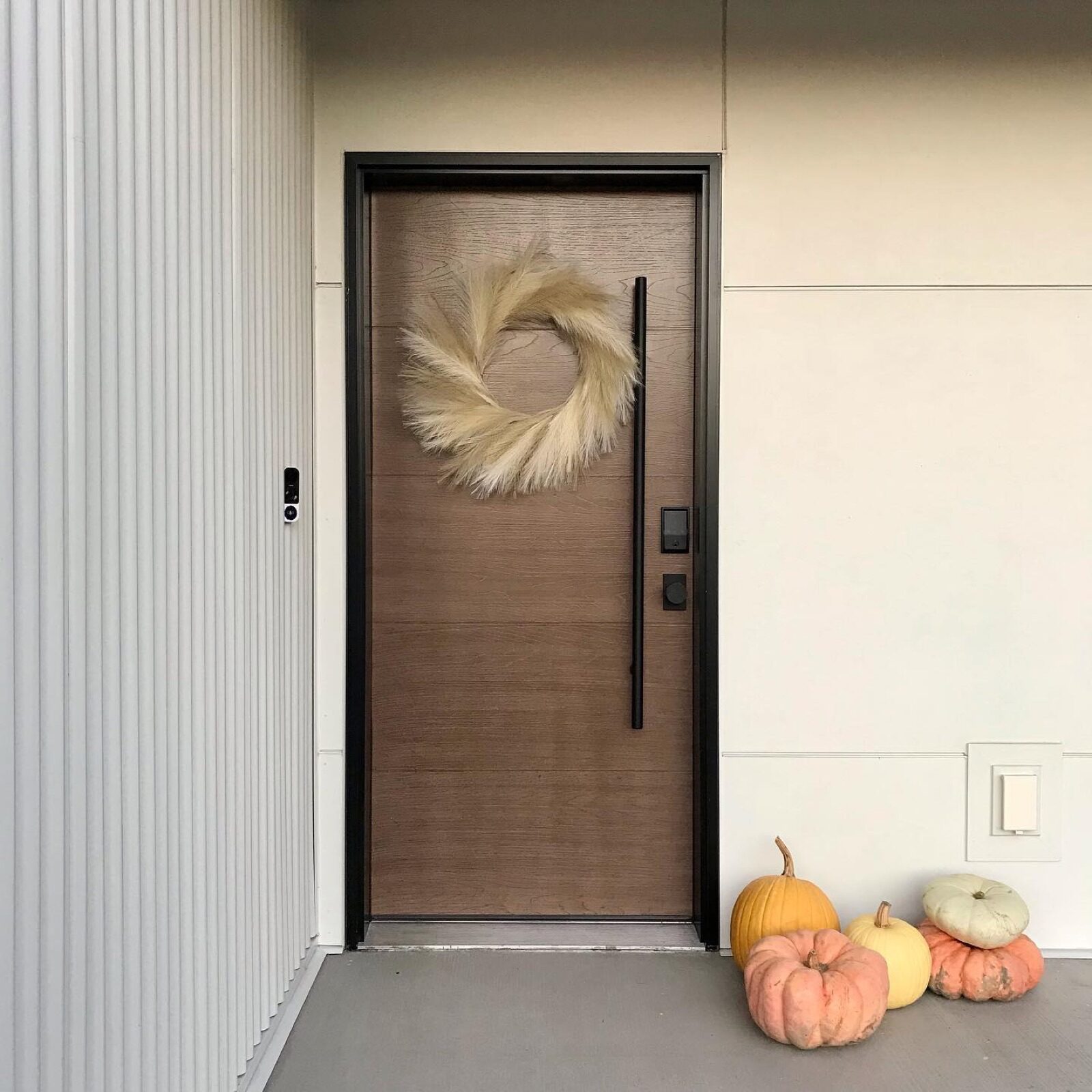 A Therma-Tru wooden front door accented by a feathery wreath, with a small pile of assorted pumpkins on the porch.