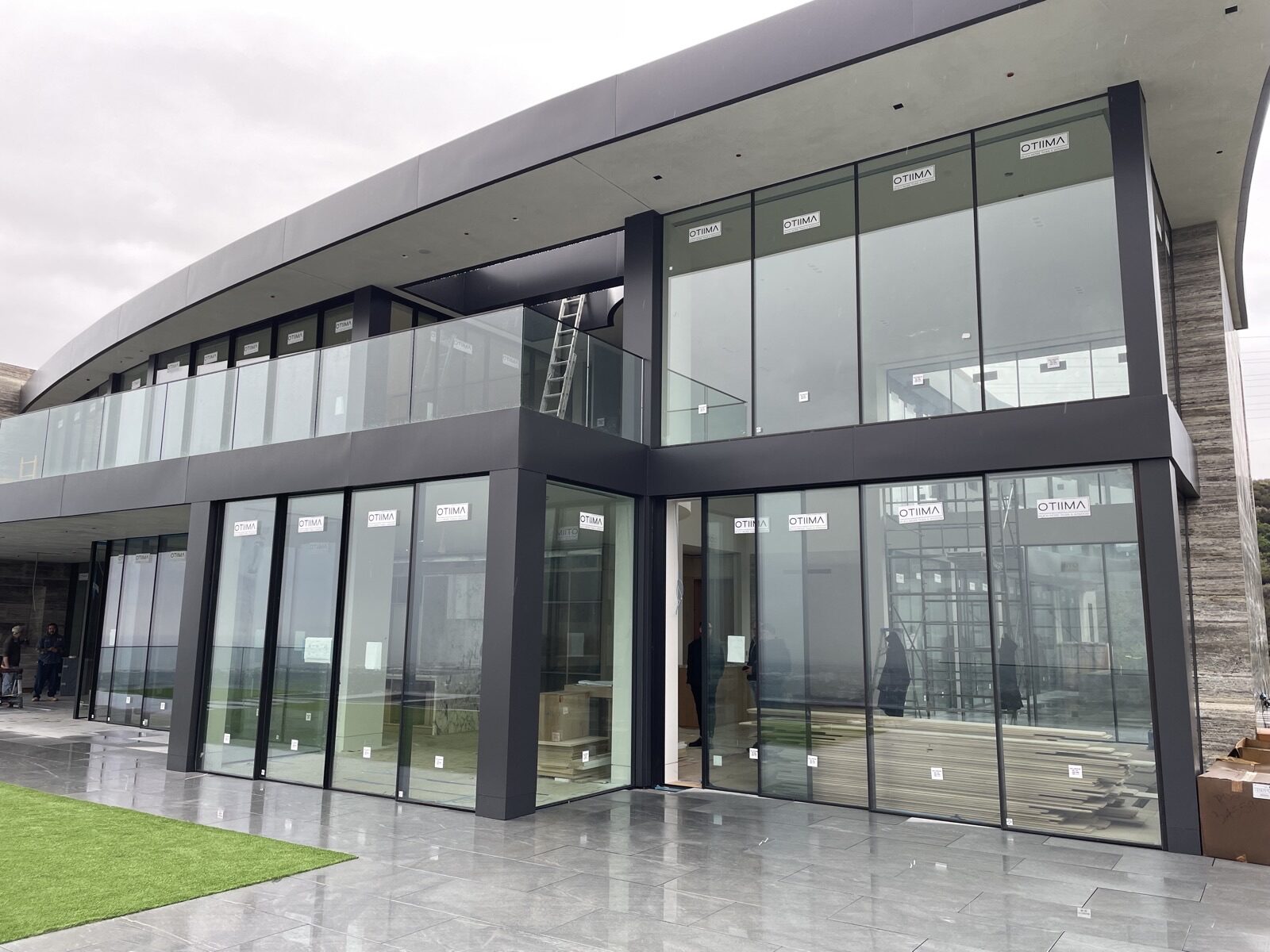 Modern two-story Titoni building under construction with large glass window panels labeled OTIMA.