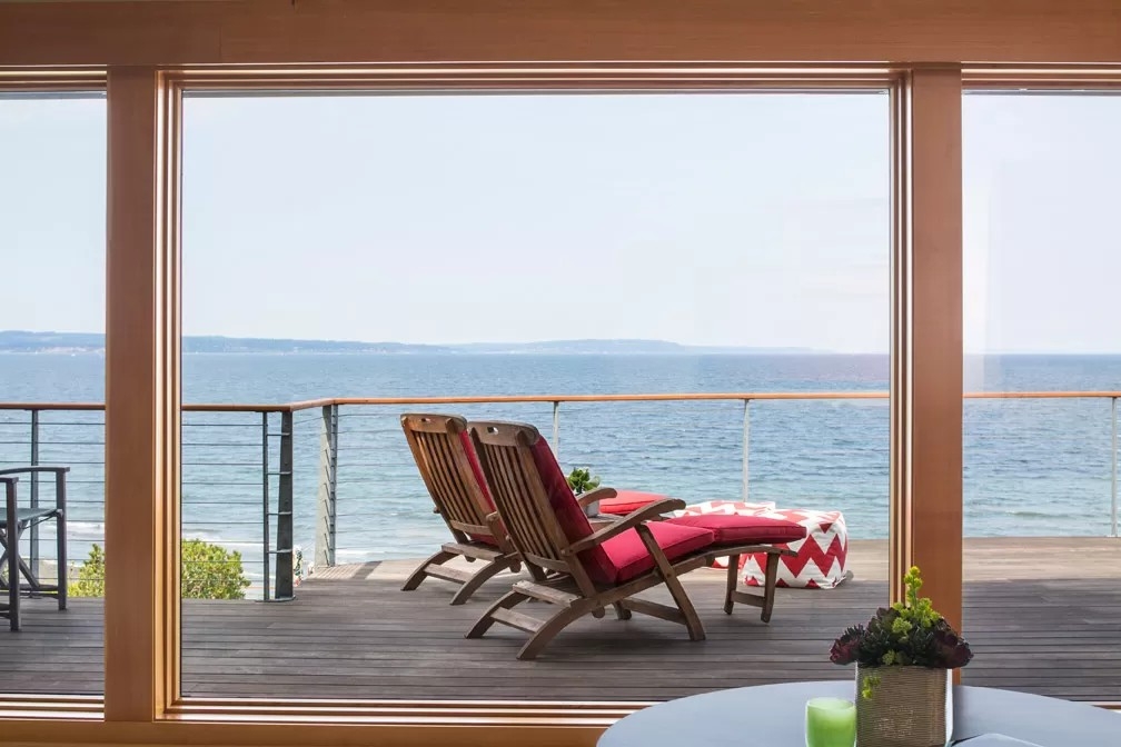 Two wooden lounge chairs with red cushions on a wooden deck overlooking the ocean at a Puget Sound home.
