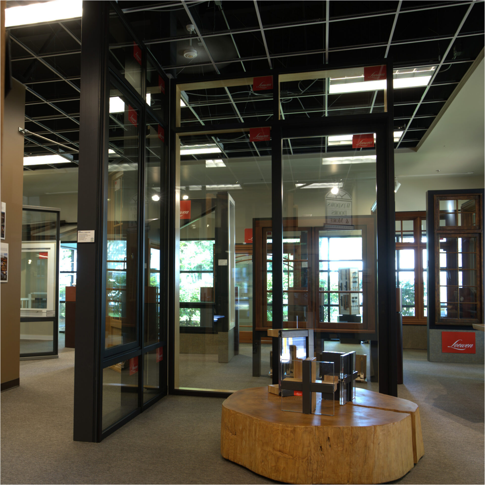 A showroom featuring various large windows, doors and more, with a wooden stump table in the foreground holding small product samples.