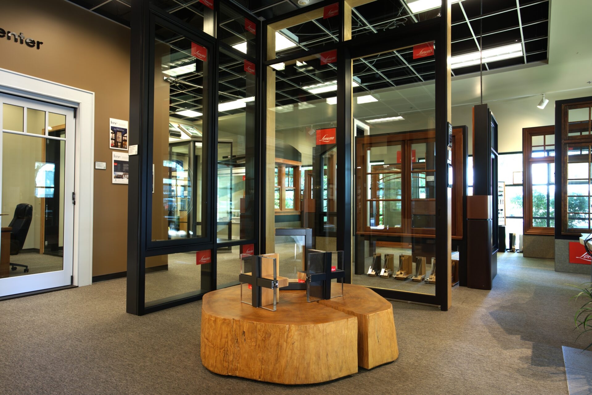 A showroom display of windows doors and more, featuring various frames with a cross-section sample resting on a large wooden stump table.