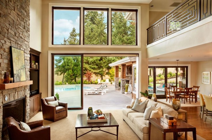 Living room with a stone fireplace, leather armchairs, and a sofa facing Milgard glass doors that open to a patio with a swimming pool.